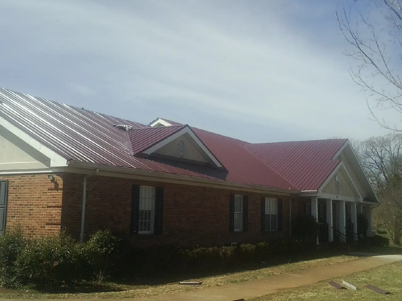 Red metal roof with gabled entries on a long brick building, from a Hail Damage Roof Repair job in Willamina